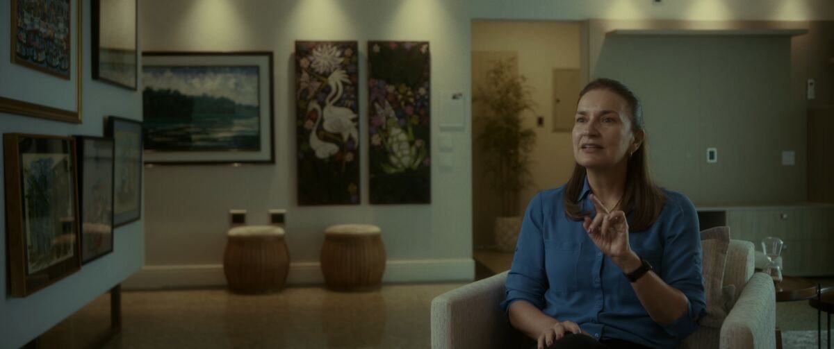 Mulher de camisa azul sentada numa poltrona, falando para a câmera, em cena do documentário Um Shabat na Outra Margem do Rio